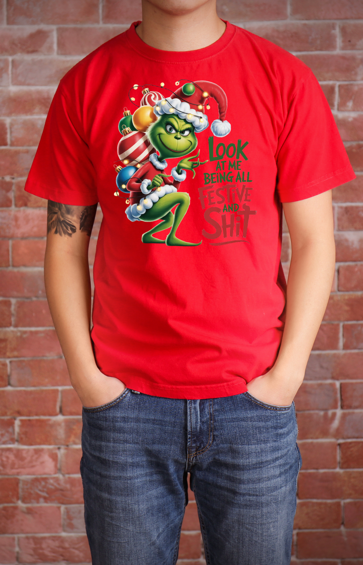 Model wearing a red Christmas T-shirt with a Grinch graphic and festive slogan