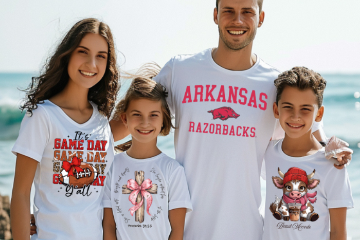 Family of four wearing white t-shirts with various designs on a beach.